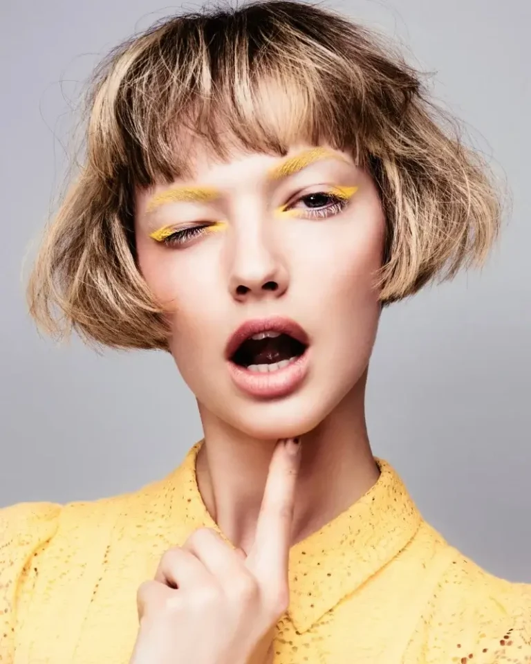 Model featuring a short blonde bob haircut with soft curled ends and straight eyebrow-skimming bangs