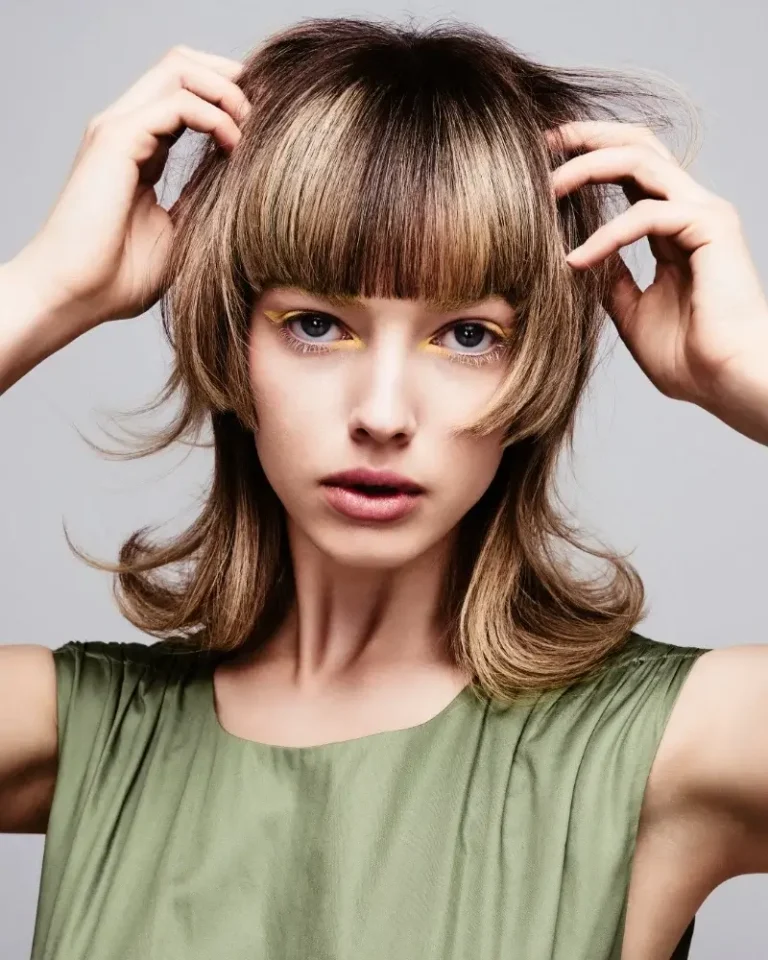 Model with straight ash-brown hair featuring framed cheek-length layers and blunt, textured bangs