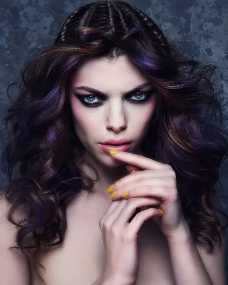Model with voluminous dark wavy hair featuring subtle purple highlights and small braids along the crown