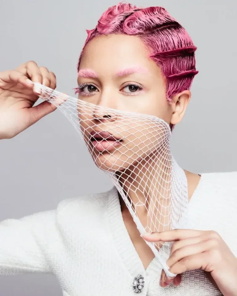 Model with a vibrant pink finger-wave haircut pulled over her face by a white fishnet veil