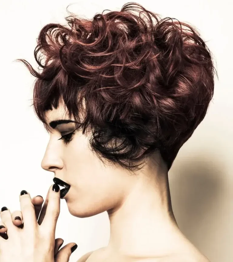 Side profile portrait of a woman with a textured auburn red short crop featuring voluminous curls and a short fringe