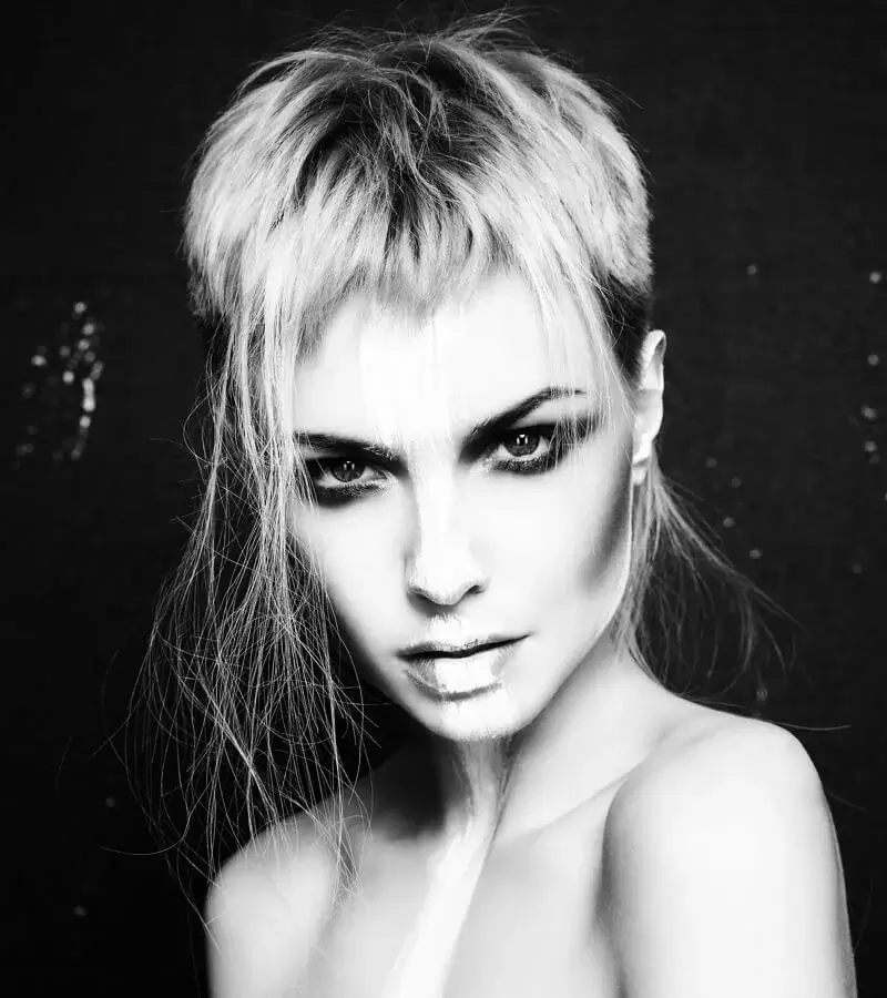 Frontal black and white portrait of a woman featuring a textured mullet crop with wispy, face-framing fringe and sharp eye makeup