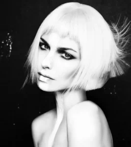 Black and white studio portrait of a woman with a sleek blonde blunt bob haircut and short micro-bangs