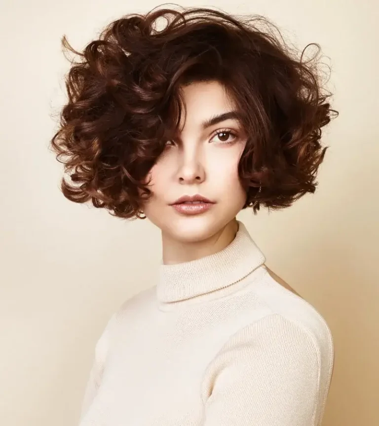 Model with a voluminous, short dark brown curly bob wearing a white turtleneck sweater